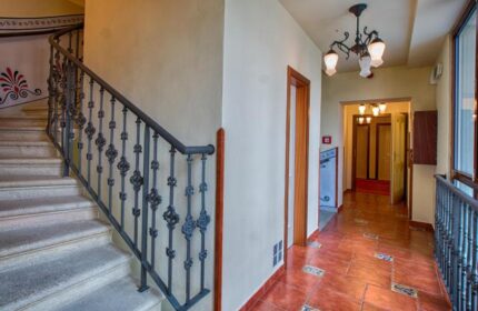 Interior of Arkada Hotel Praha, a gay-friendly hotel. View of staircase with ornate railing and hallway with tiled floor and chandelier lighting.