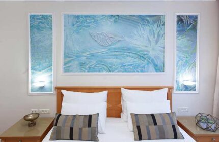 Armon Hayarkon Hotel room with sea-themed art. Gay-friendly hotel bedroom features white linens, striped pillows, and ocean-inspired wall decor.