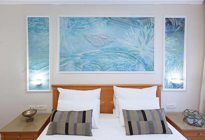 Armon Hayarkon Hotel room with sea-themed art. Gay-friendly hotel bedroom features white linens, striped pillows, and ocean-inspired wall decor.