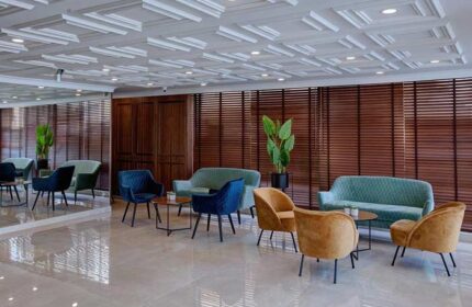 Lobby at Armon Hayarkon Hotel, a gay-friendly hotel. Seating area with sofas and chairs, wood paneling, and decorative ceiling. Modern design.