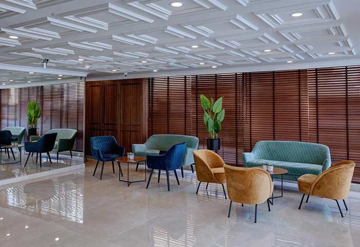 Lobby at Armon Hayarkon Hotel, a gay-friendly hotel. Seating area with sofas and chairs, wood paneling, and decorative ceiling. Modern design.