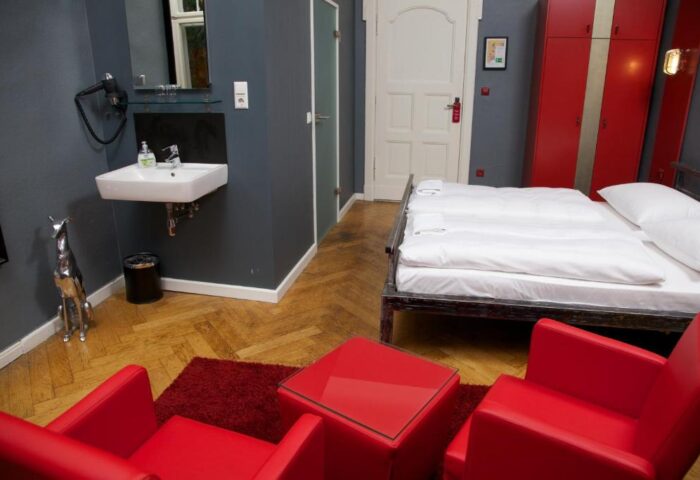 ArtHotel Connection gay-friendly hotel room. Pet-friendly room with double bed, red armchairs, sink, and red wardrobe. Stylish design.