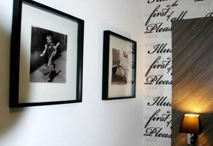 Arthotel ANA Boutique Six detail: Framed black & white art, wallpaper with text, and a lamp. Gay-friendly hotel interior design.