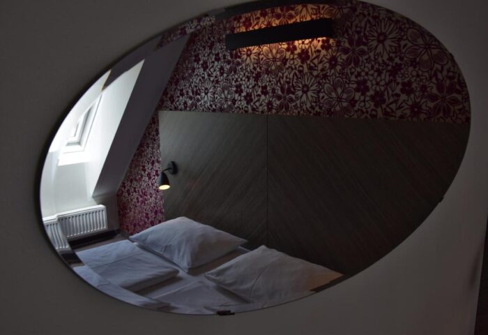 Arthotel ANA Boutique Six gay-friendly hotel room reflected in oval mirror. Cozy bed, floral wallpaper, and modern design. Gay travel.