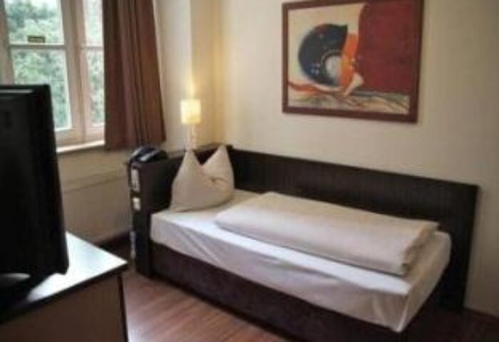 Arthotel Munich room. Gay-friendly hotel with single bed, abstract art, TV, window and brown curtains. A comfortable stay in Munich.