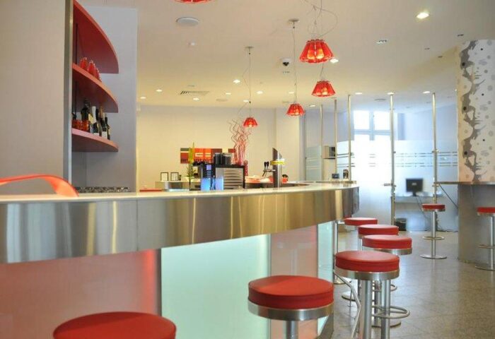 Arthotel Munich bar area. Gay-friendly hotel interior with red stools, modern lighting, and a sleek bar. A comfortable space for gay travelers.