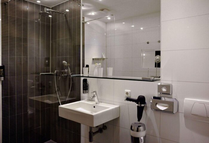 Arthotel Munich gay-friendly hotel bathroom. Features a shower with dark tiles, a sink, a mirror, and a hairdryer. Modern design.