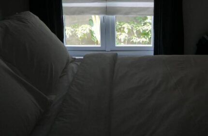 Bedroom at Arthur&Paul, a gay-friendly men-only hotel. View of a bed with white linens and pillows, window with foliage outside. Relaxing space.