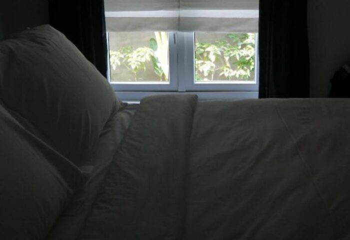 Bedroom at Arthur&Paul, a gay-friendly men-only hotel. View of a bed with white linens and pillows, window with foliage outside. Relaxing space.