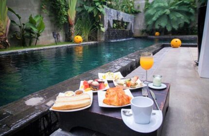 Breakfast by the pool at Arthur&Paul, a gay-friendly men-only hotel. Enjoy toast, croissants, fruit, juice, and coffee in a lush, tropical setting.