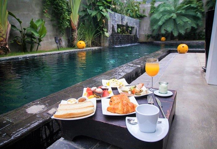 Breakfast by the pool at Arthur&Paul, a gay-friendly men-only hotel. Enjoy toast, croissants, fruit, juice, and coffee in a lush, tropical setting.