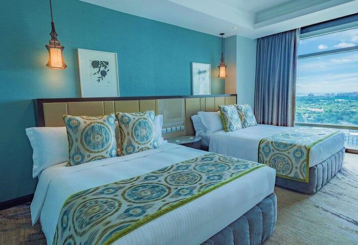 Ascott Makati gay-friendly hotel room with two beds, blue accent wall, city view. Upscale accommodations for gay travelers in Makati, Philippines.