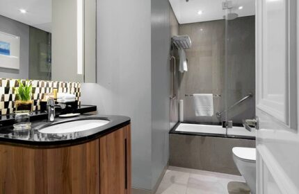 Ascott Makati gay-friendly hotel bathroom. Modern design with wood vanity, black countertop, and shower-tub combo. Accessible features.