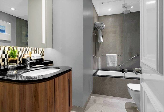 Ascott Makati gay-friendly hotel bathroom. Modern design with wood vanity, black countertop, and shower-tub combo. Accessible features.