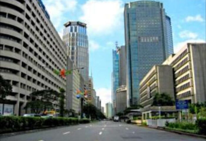 Street view of Ascott Makati, a gay-friendly hotel in Makati, Philippines. Tall buildings line the street under a blue sky. Urban travel destination.