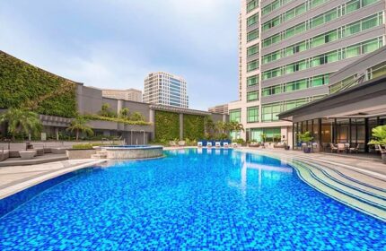 Ascott Makati gay-friendly hotel pool. Blue tiled pool with lounge seating, plants, and a tall building. A great spot for gay travelers.