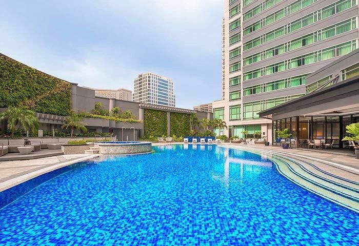 Ascott Makati gay-friendly hotel pool. Blue tiled pool with lounge seating, plants, and a tall building. A great spot for gay travelers.