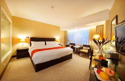 Gay-Friendly Asia Hotel room. Modern decor, king-size bed with orange accent, sitting area, fruit plate. Ideal for gay travelers in Asia.