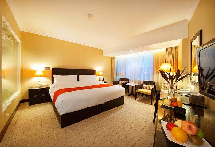 Gay-Friendly Asia Hotel room. Modern decor, king-size bed with orange accent, sitting area, fruit plate. Ideal for gay travelers in Asia.