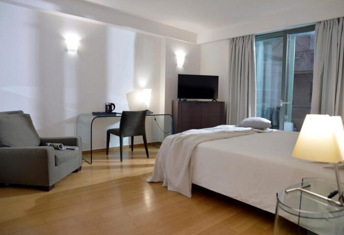 Athenaeum Eridanus Luxury Hotel room. Gay-friendly hotel with bed, desk, chair, TV, and balcony. Modern interior design.