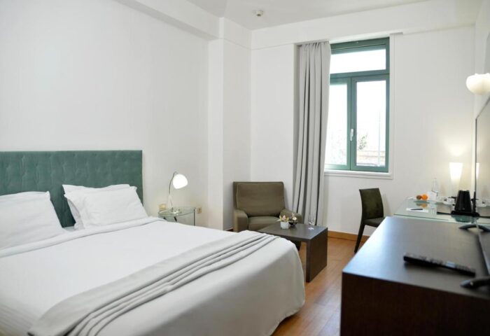 Athenaeum Eridanus Luxury Hotel room. Gay-friendly hotel featuring a bed with white linens, a chair, a desk, and a window. Athens hotel.