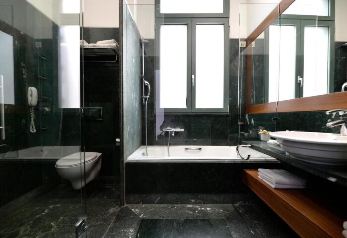Bathroom at Athenaeum Eridanus Luxury Hotel, a gay-friendly hotel. Features marble, glass shower, tub, sink, and window. Upscale design.