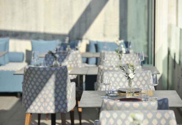 Athenaeum Eridanus Luxury Hotel's gay-friendly restaurant. Tables are set with glassware and flowers. Blue cushions accent the seating.