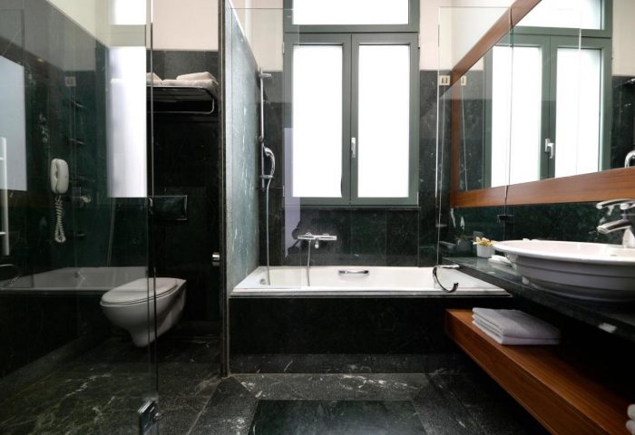 Bathroom at Athenaeum Eridanus Luxury Hotel, a gay-friendly hotel. Features tub, shower, toilet, sink, and dark marble. Gay travel advice.