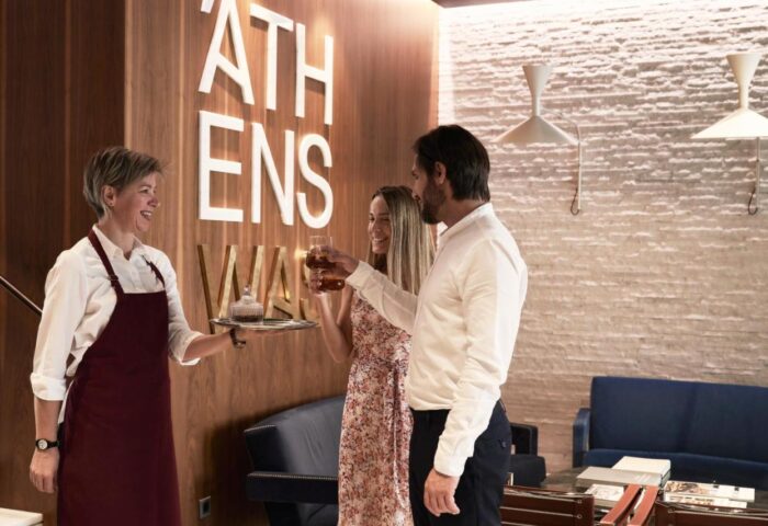 AthensWas Hotel: Couple toasting drinks served by staff. Gay-friendly hotel in Athens offers a welcoming experience. Modern interior design.