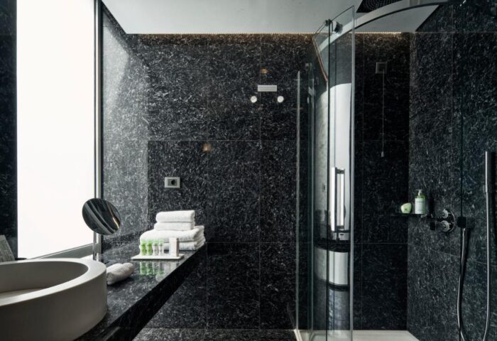 AthensWas Hotel's modern, gay-friendly bathroom. Dark marble, shower, sink, and towels create a luxurious experience for gay travelers.