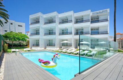 Atlantic Sun Beach, gay men only hotel, with pool and unicorn float. Gay-friendly hotel exterior, white building, sunny day.