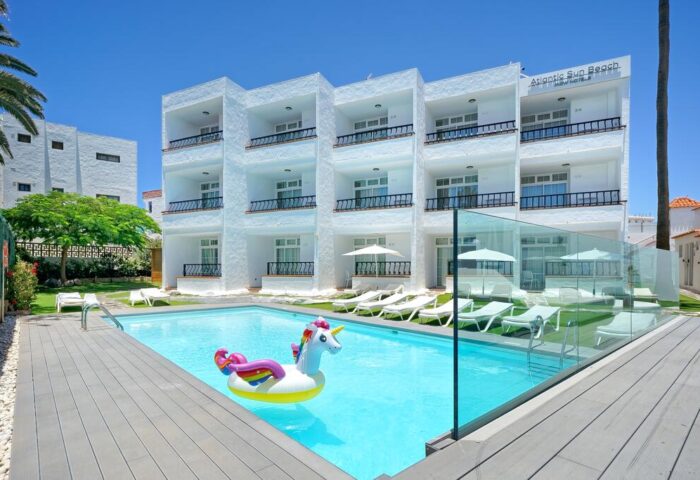 Atlantic Sun Beach, gay men only hotel, with pool and unicorn float. Gay-friendly hotel exterior, white building, sunny day.