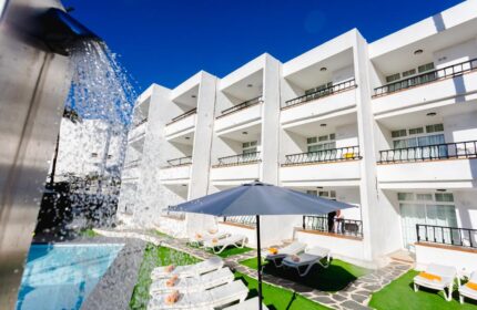 Atlantic Sun Beach gay men only hotel. White building with balconies, pool, lounge chairs, and umbrella. Gay-friendly hotel for gay men.