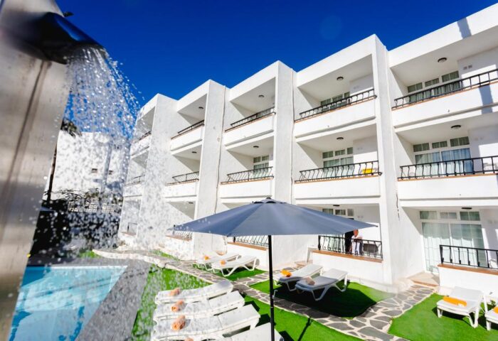 Atlantic Sun Beach gay men only hotel. White building with balconies, pool, lounge chairs, and umbrella. Gay-friendly hotel for gay men.