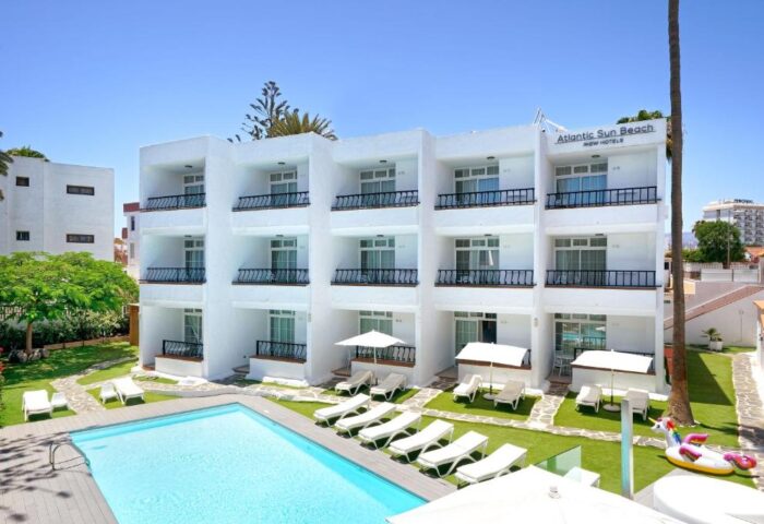 Atlantic Sun Beach, a gay-friendly hotel. White building with balconies, pool, sunbeds, and a unicorn float. Perfect for gay men's travel.