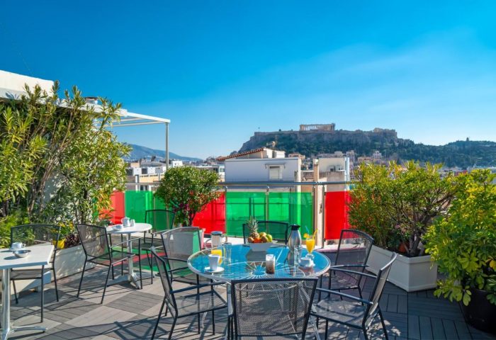 Attalos Hotel rooftop terrace view of Acropolis. Gay-friendly hotel in Athens, Greece. Outdoor seating and clear blue sky.