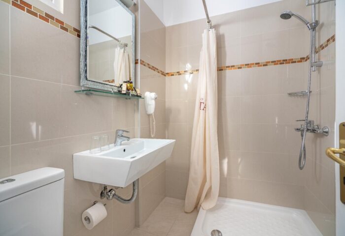 Attalos Hotel gay-friendly bathroom. Modern sink, shower with curtain, mirror, and toilet. Comfortable amenities for gay travelers.