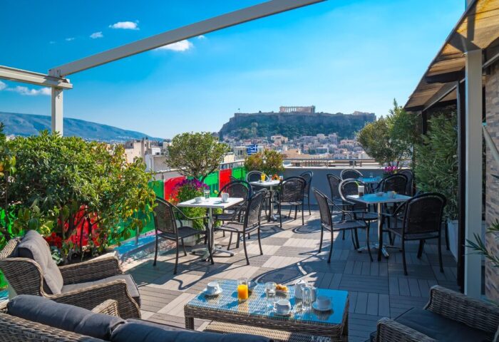 Attalos Hotel's rooftop terrace, a gay-friendly hotel, offers Acropolis views. Tables and chairs are set for breakfast in Athens, Greece.