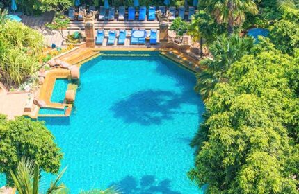 Aerial view of the pool at Avani Pattaya Resort, a gay-friendly hotel. Blue lounge chairs surround the pool amid lush greenery.