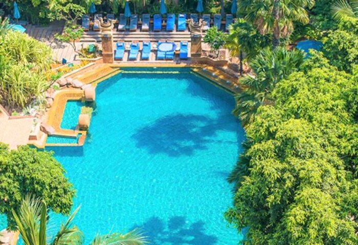 Aerial view of the pool at Avani Pattaya Resort, a gay-friendly hotel. Blue lounge chairs surround the pool amid lush greenery.