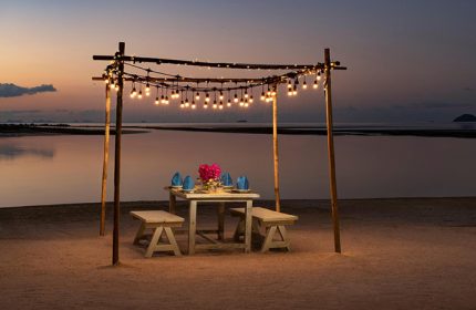 Romantic beach dinner at Avani+ Samui Resort, a gay-friendly hotel. Sunset dining with string lights, perfect for LGBTQ+ couples' getaway.
