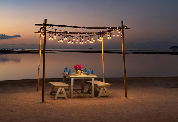 Romantic beach dinner at Avani+ Samui Resort, a gay-friendly hotel. Sunset dining with string lights, perfect for LGBTQ+ couples' getaway.