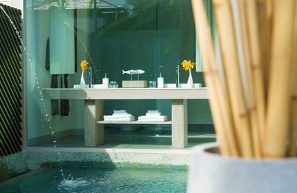 Avani+ Samui Resort's gay-friendly hotel bathroom. A double vanity with towels sits beside a pool. Yellow flowers add a pop of color.