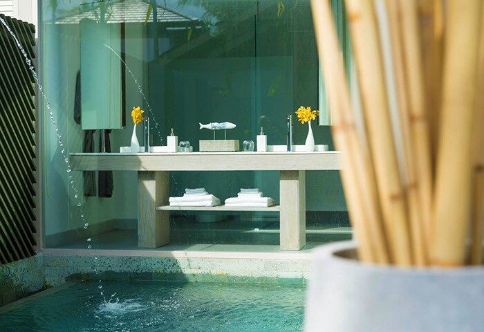Avani+ Samui Resort's gay-friendly hotel bathroom. A double vanity with towels sits beside a pool. Yellow flowers add a pop of color.