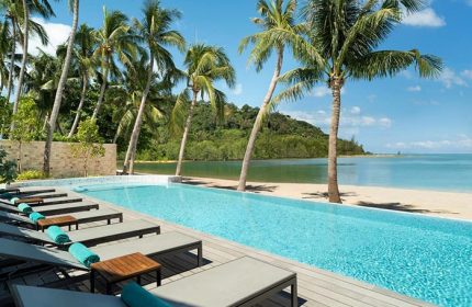 Avani+ Samui Resort's pool, a gay-friendly hotel. Palm trees line the beach. Lounge chairs await guests at this tropical paradise.