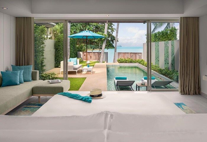 Avani+ Samui Resort gay-friendly hotel room view. Pool, lounge chairs, ocean, and patio furniture visible from the room. Tropical getaway.