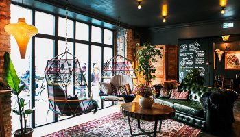 Axel Guldsmeden gay-friendly hotel lounge area. Hanging chairs, green leather sofa, rug, and plants create a cozy, stylish space for gay travelers.