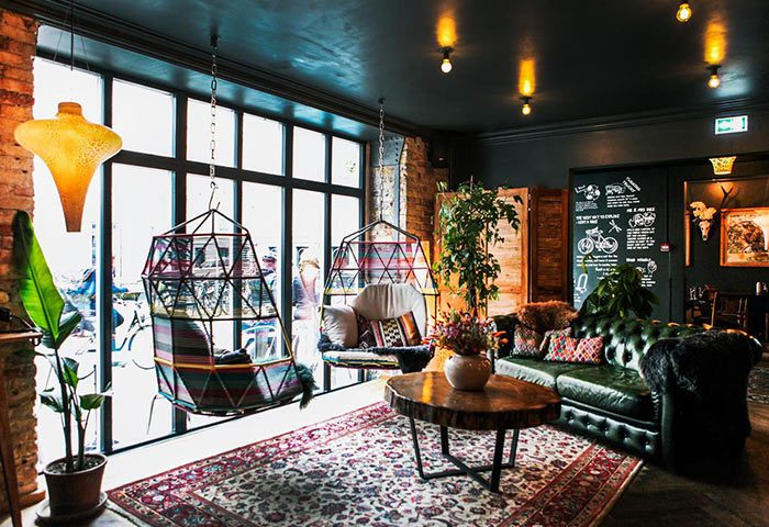 Axel Guldsmeden gay-friendly hotel lounge area. Hanging chairs, green leather sofa, rug, and plants create a cozy, stylish space for gay travelers.