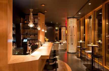Axel Hotel Berlin-Adults Only gay-friendly hotel bar. Modern design with wood accents, pendant lights, and tables. Gay travel advice.