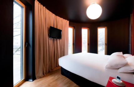 Bedroom at Axel Hotel Berlin, a gay-friendly hotel. Modern design with dark walls, wood floors, and large windows. Bed with white linens, TV, and curtains.